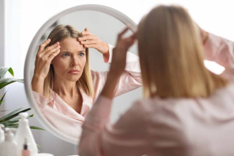 Woman looking in a mirror, examining her forehead for bruising or swelling after Botox treatment.