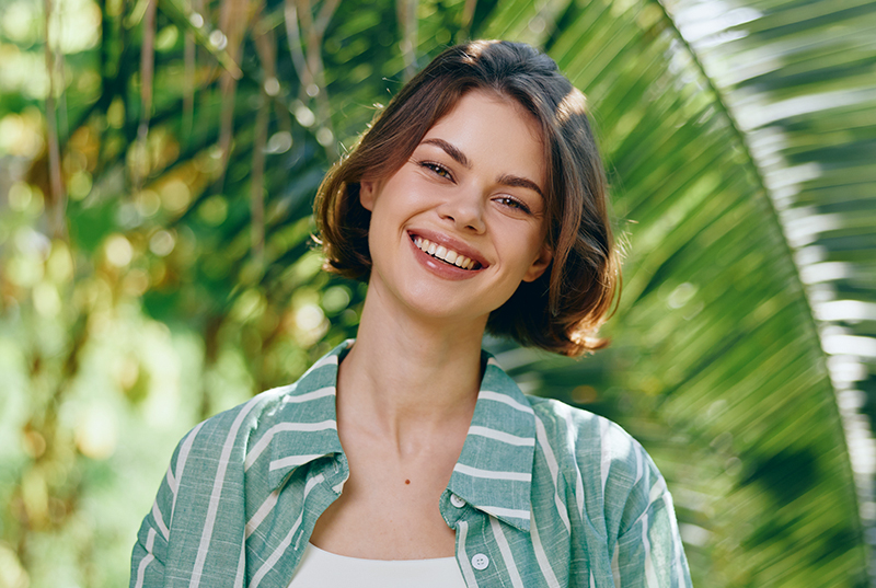 Smiling woman with balanced facial features, showcasing natural results from facial balancing treatment outdoors.