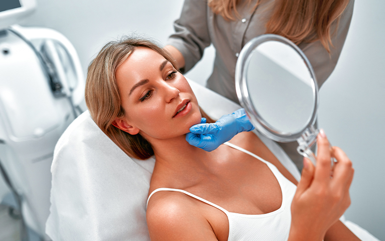 Woman examining her face in mirror during Botox consultation, with provider assessing facial movement and planning treatment