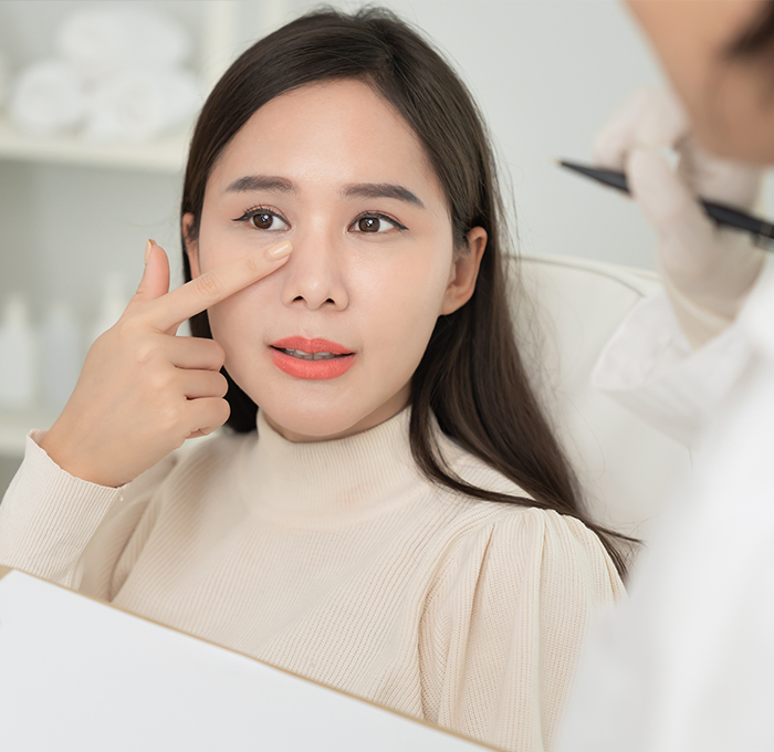 Patient pointing to her nose during a consultation, discussing concerns about nasal function and airflow related to dorsal hump correction, with a focus on preventing nasal obstruction