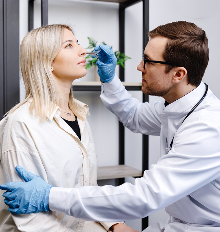 Doctor examining female patient’s nose to assess breathing issues and candidacy for functional rhinoplasty treatment