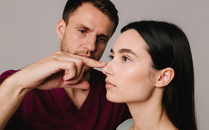 Surgeon examining a patient's nose to discuss open rhinoplasty for dorsal hump correction, highlighting the benefits of direct visualization for precise adjustments