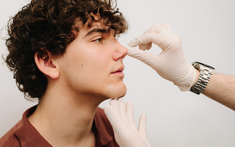 Male patient during rhinoplasty consultation with surgeon assessing nose shape to enhance overall facial proportion