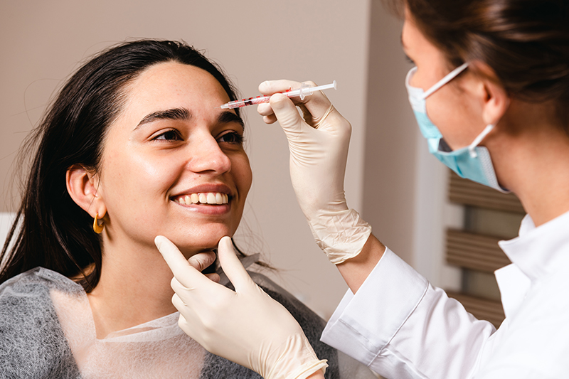 Female patient receiving Botox injection on forehead by medical professional wearing gloves and mask
