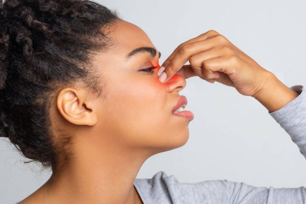 Woman pinching bridge of nose with highlighted sinus area, illustrating structural nasal obstruction versus temporary swelling