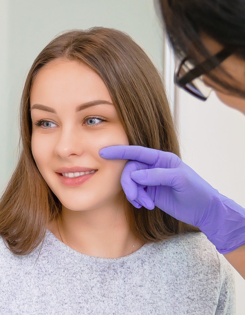 Surgeon evaluating patient’s cheek during facial liposuction consultation in New Jersey and Philadelphia office.