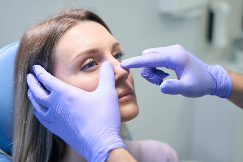 Surgeon evaluating patient’s nose during consultation for functional vs cosmetic rhinoplasty procedure planning.