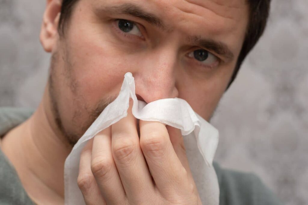 Man holding tissue to nose, representing nasal congestion, nosebleeds, and breathing difficulty from deviated septum