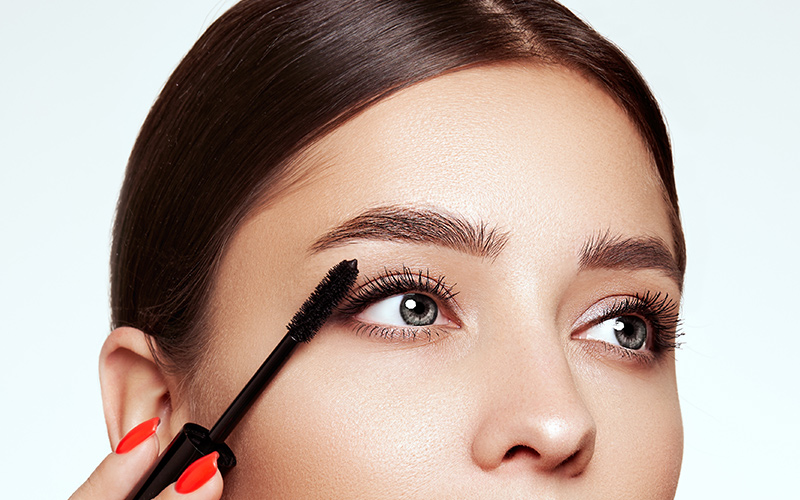 Woman applying mascara, representing enhanced lashes with Latisse treatment.