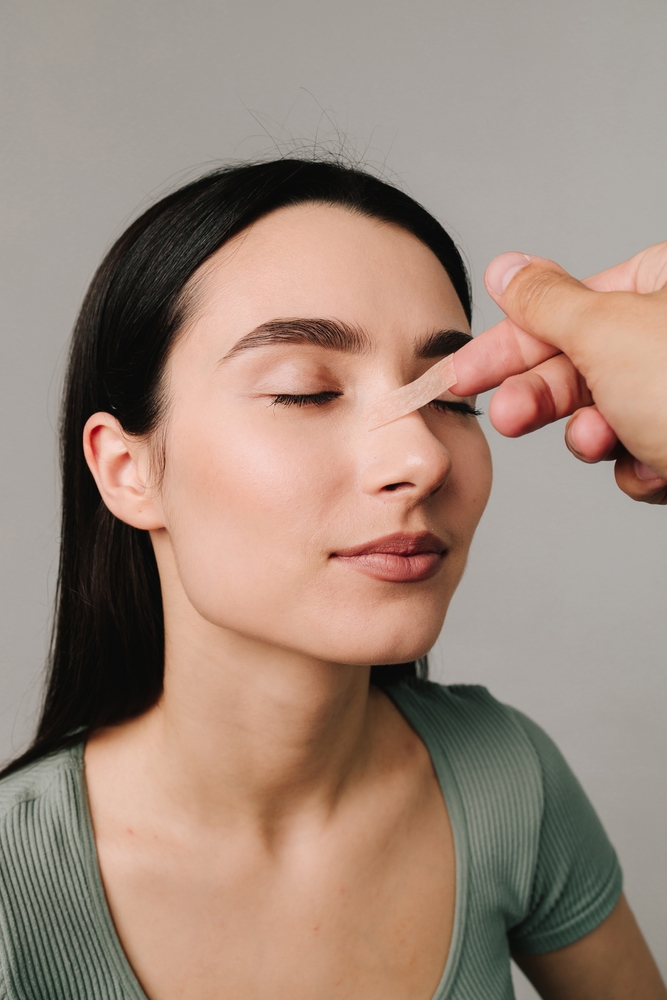 Surgeon examining patient's nose during rhinoplasty consultation to assess structure and breathing function.