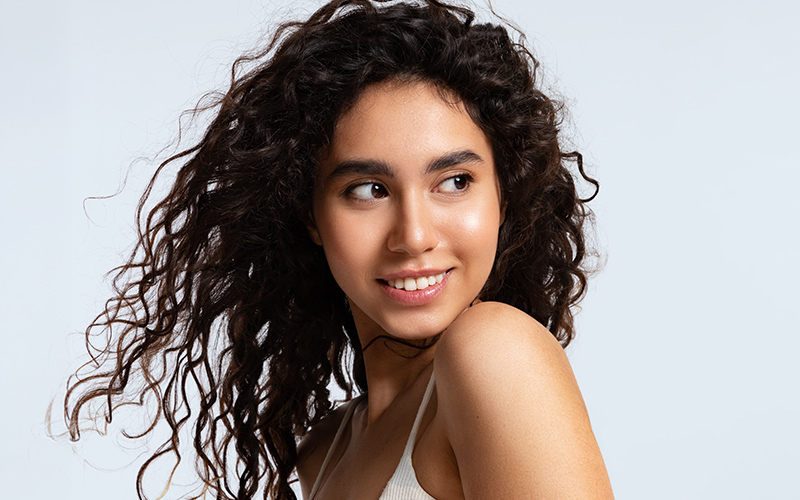 Woman with clear, glowing skin and curly hair, representing results of Clear + Brilliant laser skin rejuvenation treatment.
