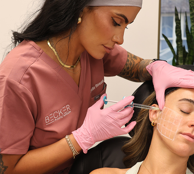 Provider administering dermal filler to cheek with marked injection grid for precise facial contouring.