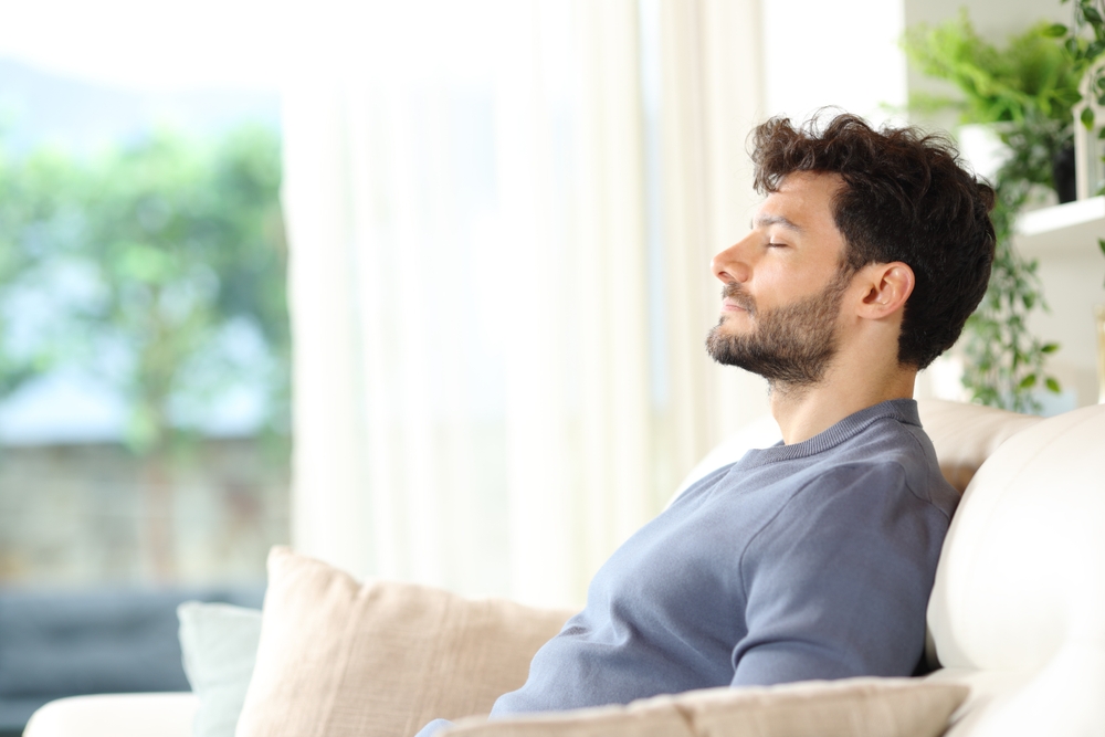 Man sitting on couch breathing comfortably, illustrating healthy nasal airflow and respiratory function.