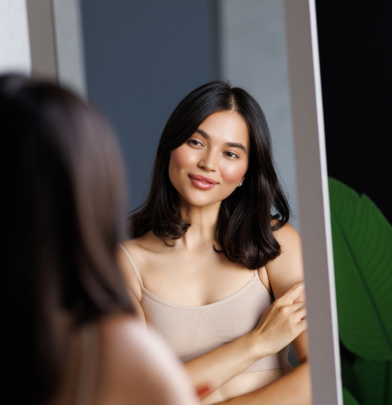 Woman reviewing her appearance in mirror during consultation about breast augmentation candidacy and expectations