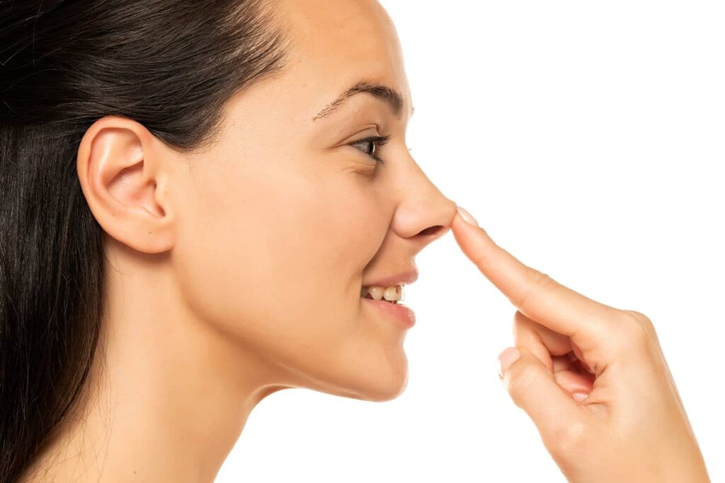 A profile view of a woman smiling while touching the tip of her nose, demonstrating an assessment for non-surgical contouring.