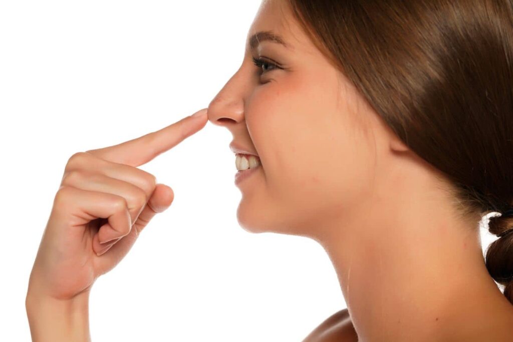 Woman pointing at nose illustrating liquid rhinoplasty vs traditional rhinoplasty treatment options and facial balance.