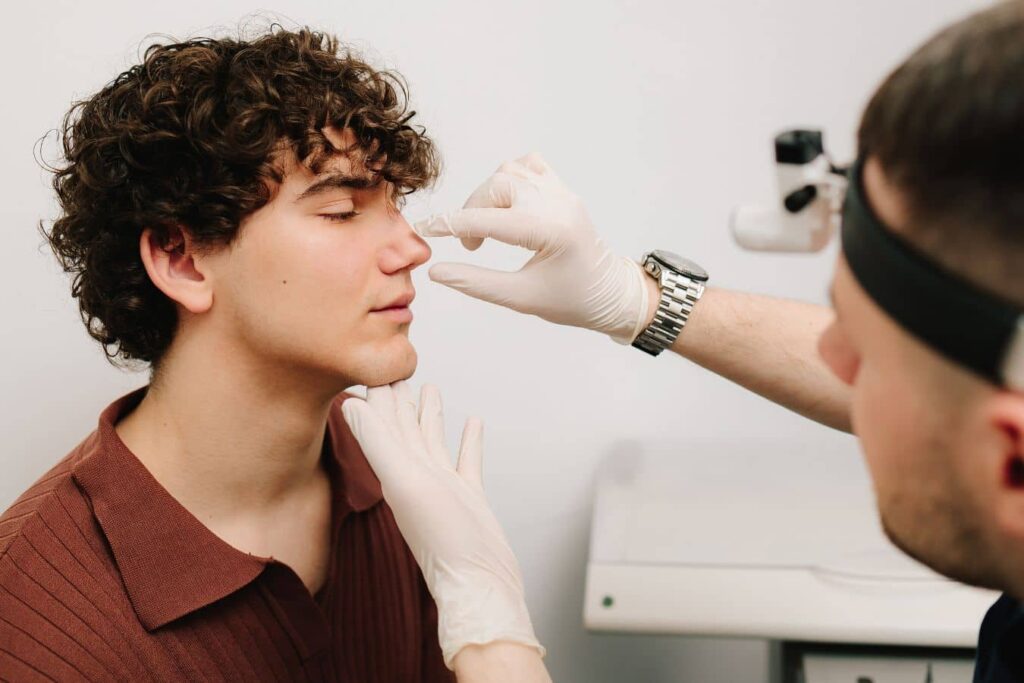 Surgeon examining patient’s nose during rhinoplasty consultation for cosmetic and functional treatment planning.
