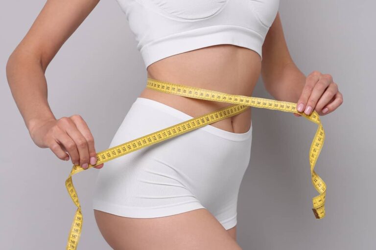 A close-up profile view of a woman in white undergarments wrapping a yellow measuring tape around her slender waist.
