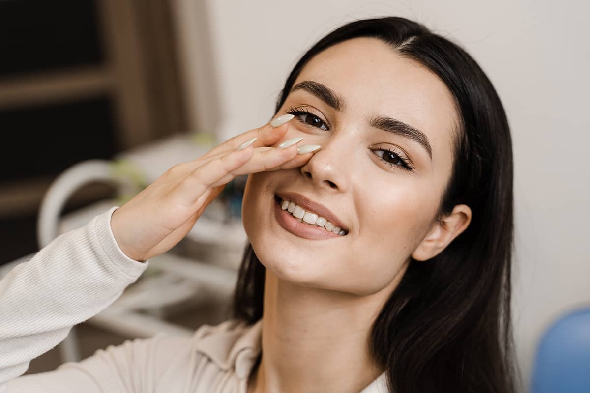 A smiling brunette woman looking forward while gently resting her fingers alongside the bridge of her nose.